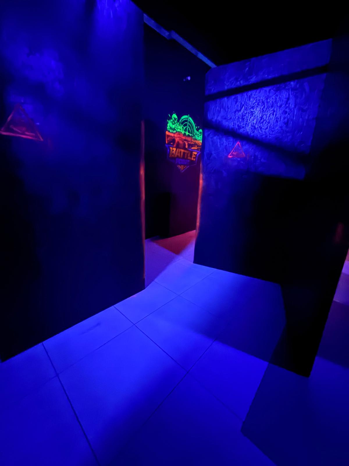 Korytarz areny laser tag z podświetleniem UV, niebieska podłoga i logo Battle Point w tle
