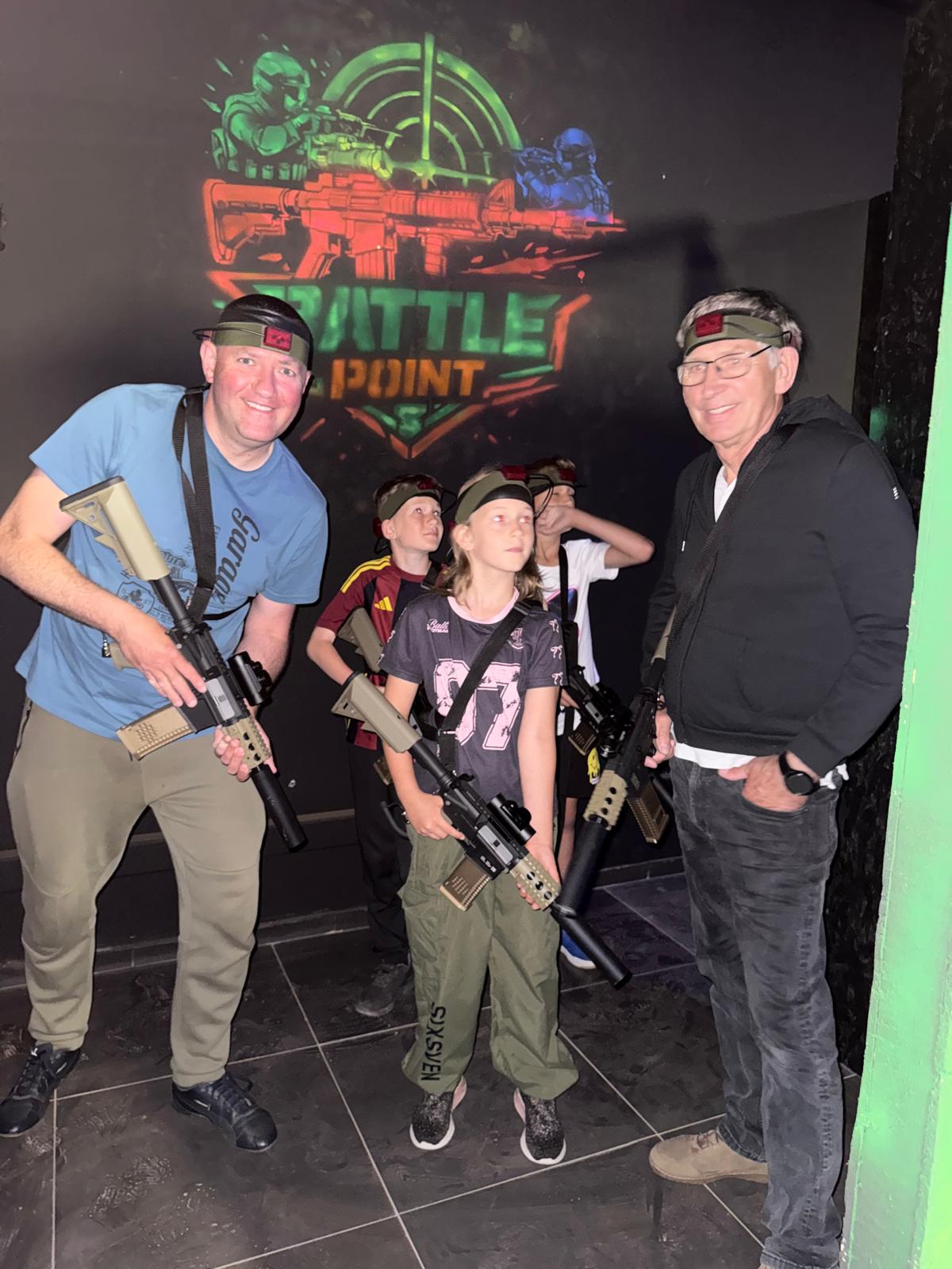 Rodzina – dorośli i dzieci – trzymający karabiny laser tag przed logo Battle Point